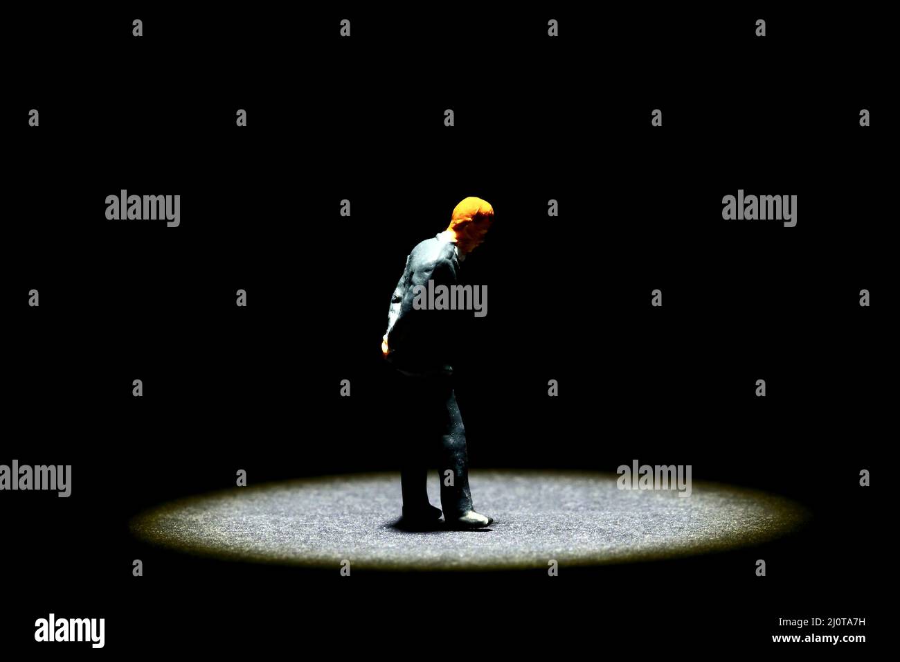 Homme miniature de figure debout dans un spot entouré de ténèbres, la santé mentale dans le besoin d'un concept de main d'aide Banque D'Images