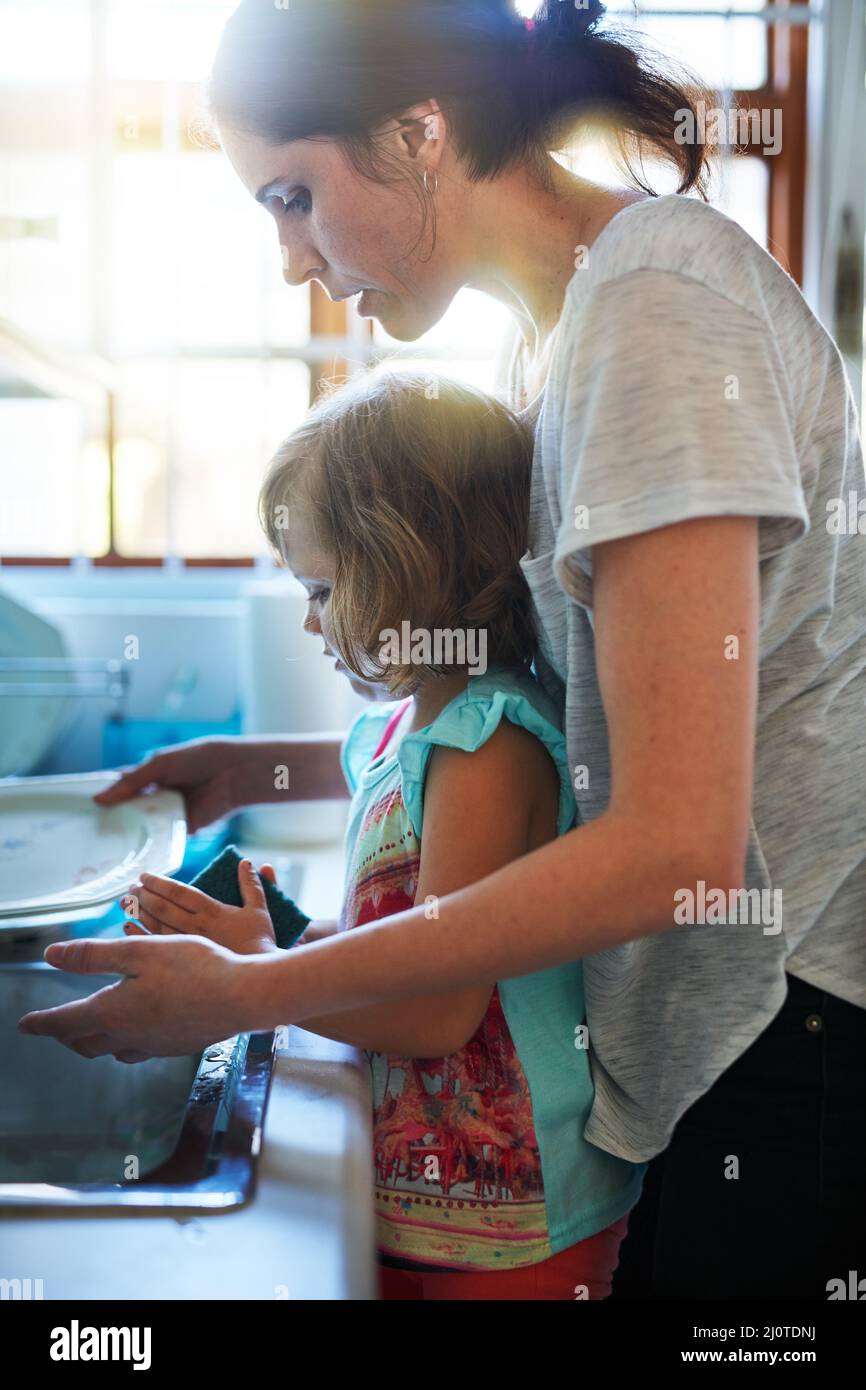 Aider à nettoyer la vaisselle. Prise de vue d'une mère et d'une fille qui lave les plats ensemble. Banque D'Images