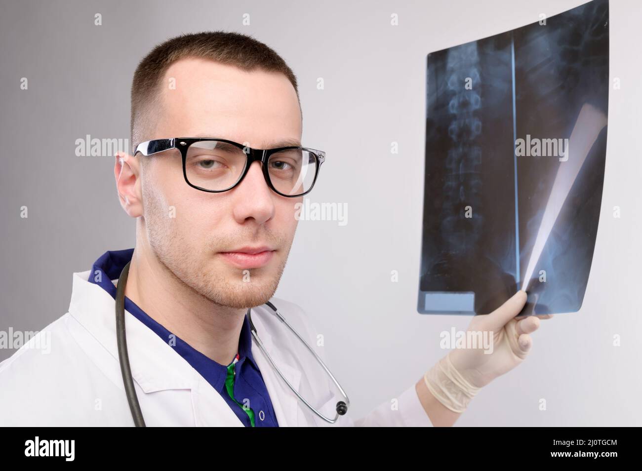 Un jeune radiologue de médecin caucasien tient une image radiographique dans sa main et regarde dans la caméra. Un homme en lunettes et un uniforme Banque D'Images