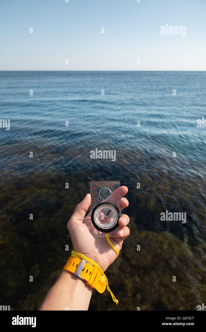 La main d'un homme avec bracelet montre tient un compas magnétique sur le fond de la mer Banque D'Images