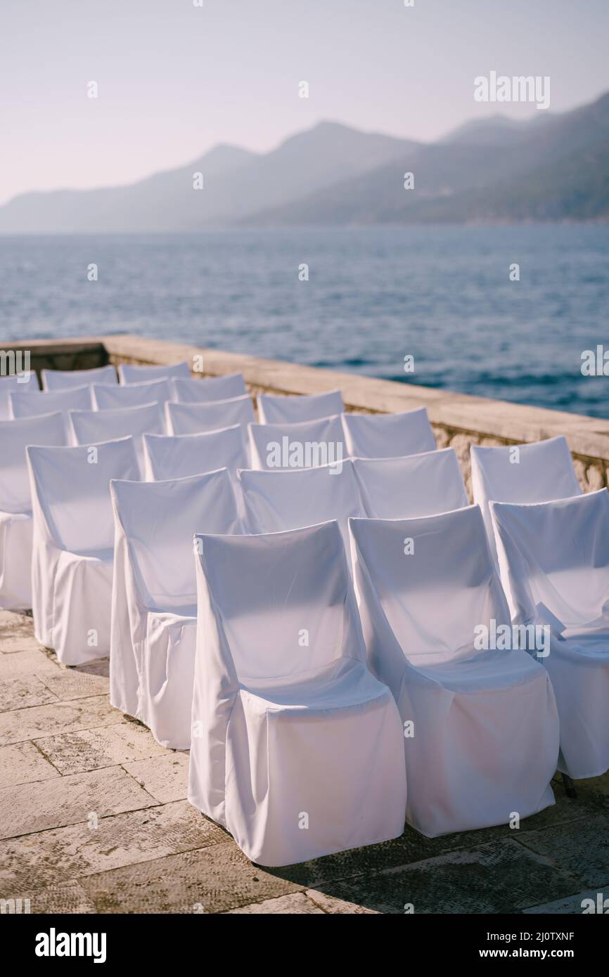 Une rangée de chaises en tissu blanc couvre des supports près d'une clôture en pierre sur le bord de mer Banque D'Images