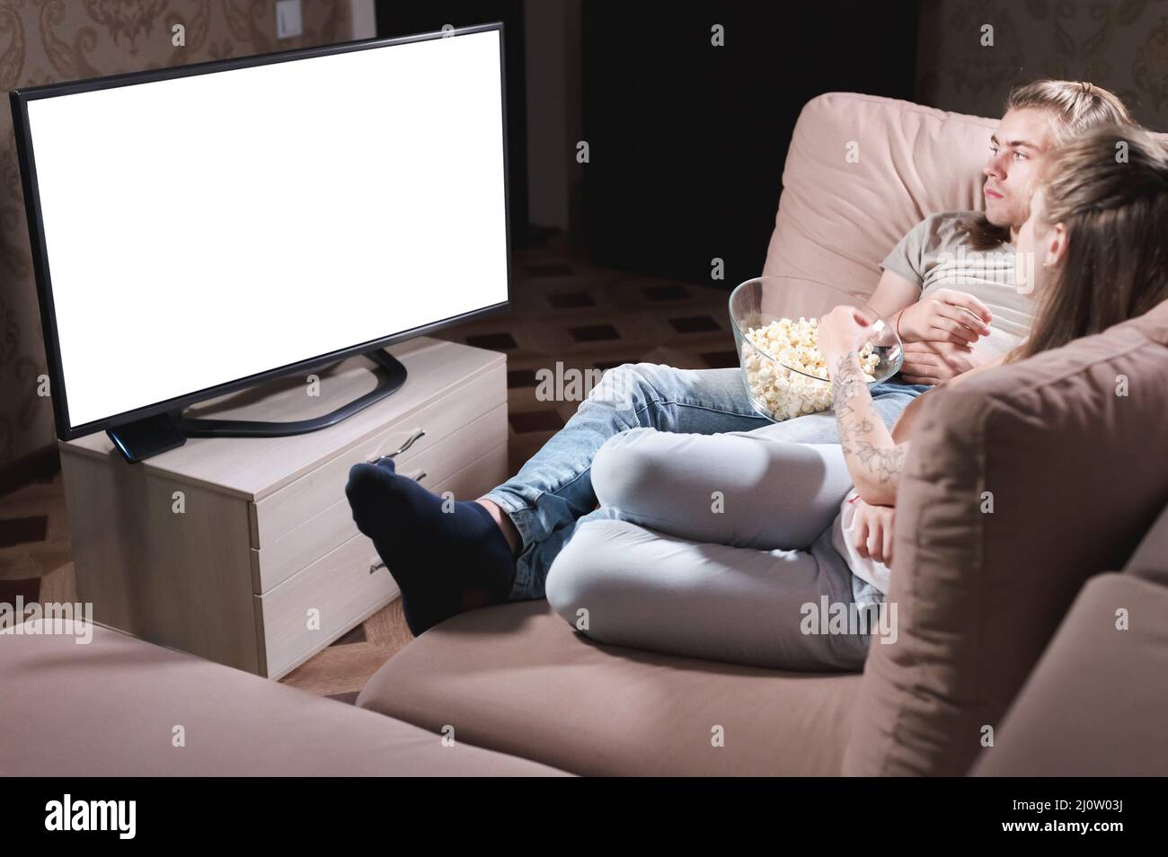 Un jeune couple attrayant aux cheveux longs qui se hante sur un canapé à la maison en regardant la télévision. Le concept de passer du temps avec l'amour Banque D'Images