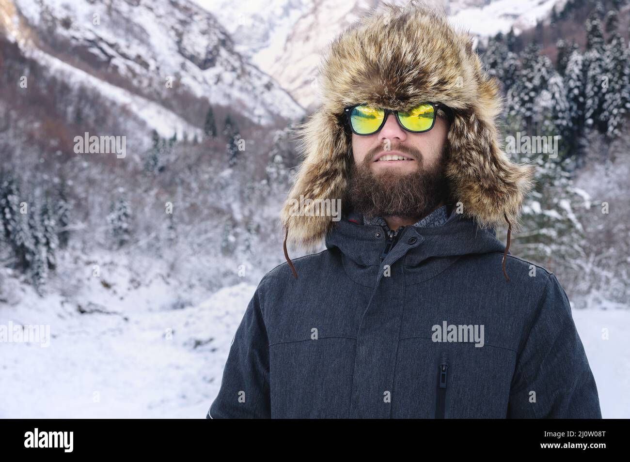 Portrait d'un jeune barbu attrayant dans un grand chapeau de fourrure et  des lunettes de soleil contre la forêt enneigée dans les montagnes Photo  Stock - Alamy
