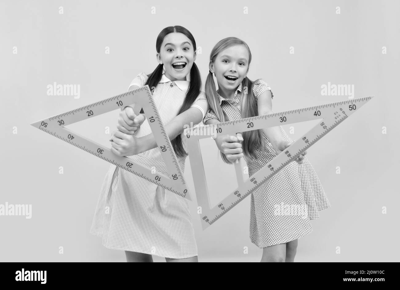 Les enfants d'âge scolaire heureux ont des règles triangulaires sur fond jaune, géométrie Banque D'Images