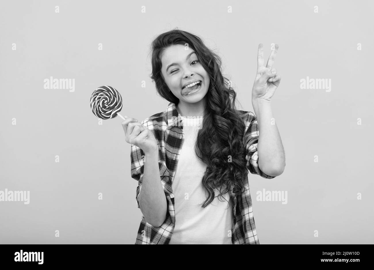 drôle de fille de l'adolescence tenir lollipop caramel bonbon sur fond jaune montrer le geste de paix, boutique de caramel. Banque D'Images