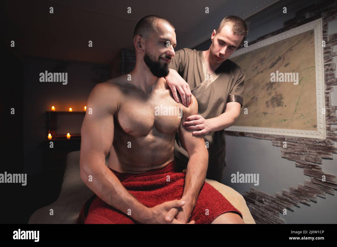 Le masseur masculin fait un massage sportif des épaules à un athlète musclé dans une pièce avec une lumière sombre contrastée. Service après-vente professionnel Banque D'Images