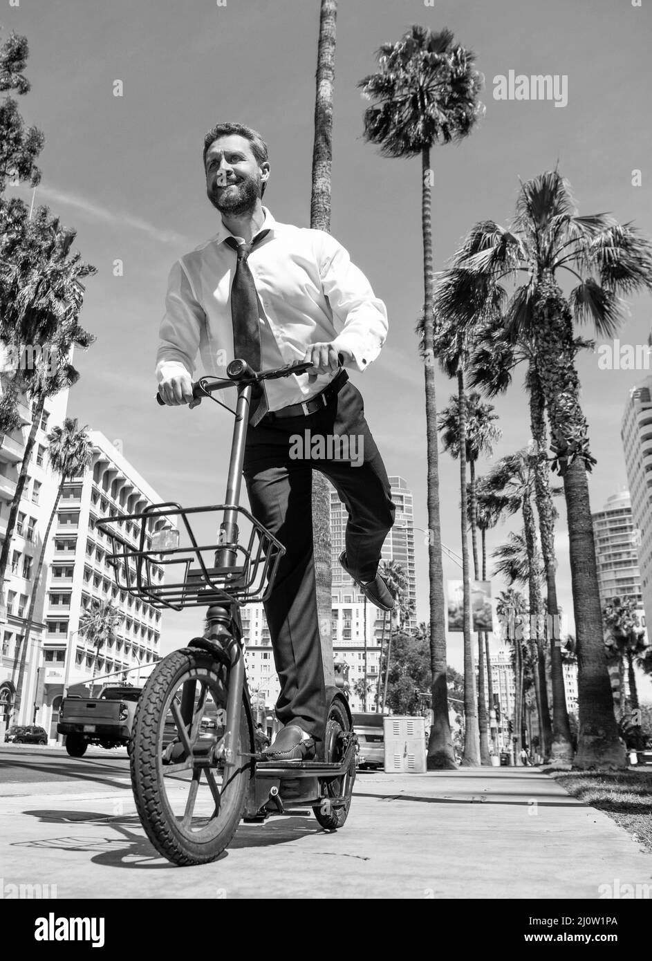 Un homme heureux en tenue de formalwear, e-scooter sur le trottoir, e-scoting Banque D'Images