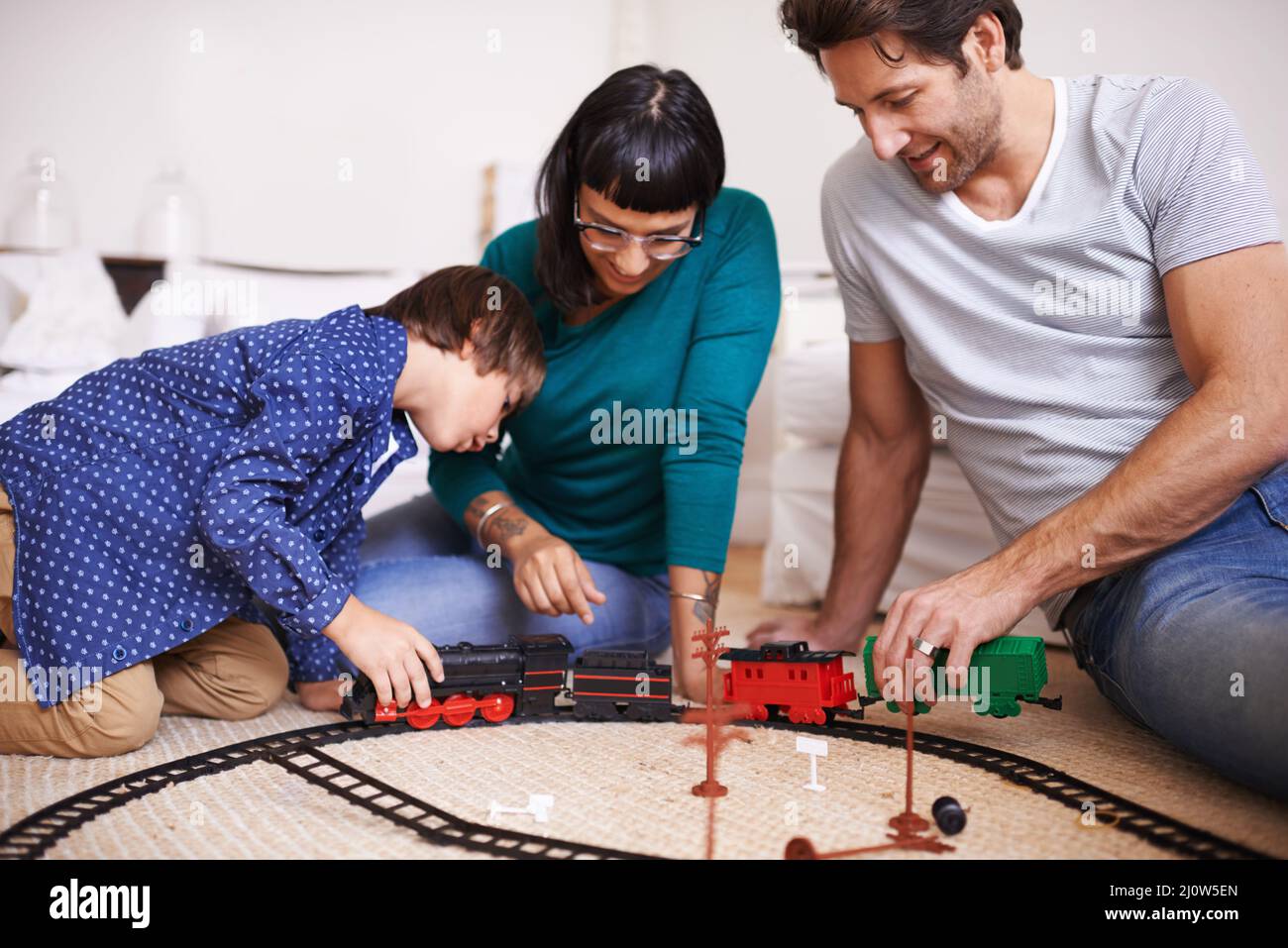 Montrant à ses parents comment accrocher le train. Photo d'une jeune famille qui a installé un train de jouets. Banque D'Images