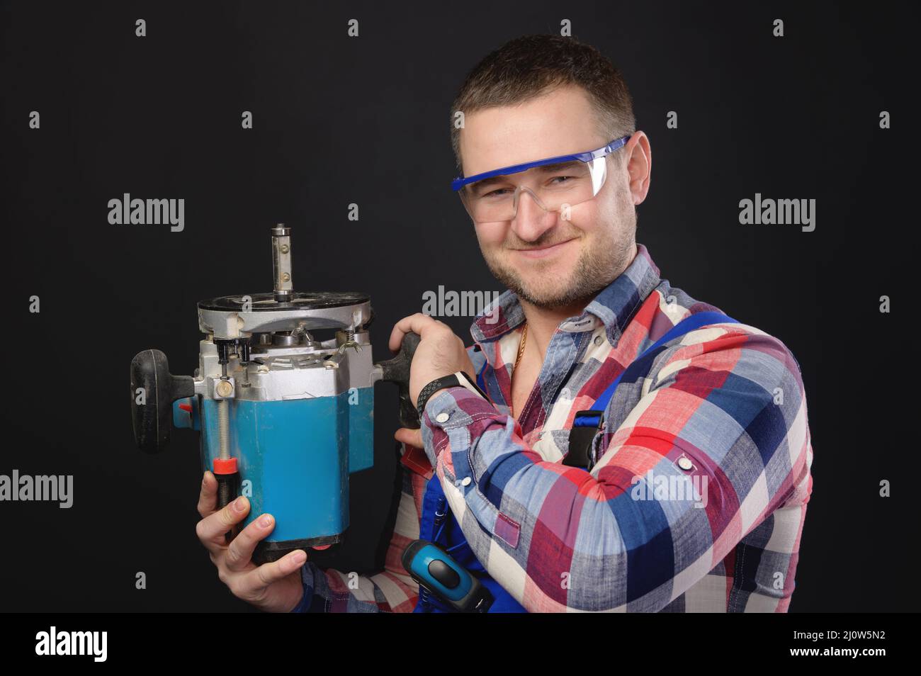 Sourire amical menuisier caucasien mâle avec un couteau à bois dans ses mains. Portrait d'un homme travaillant avec un arbre sur un dos noir Banque D'Images