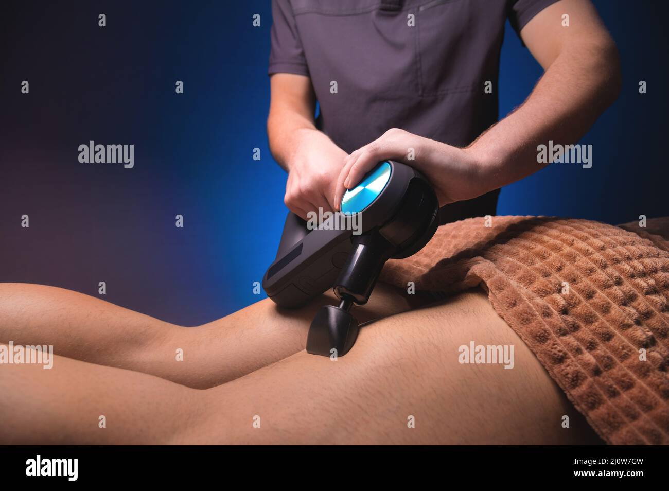Masseuse masculine effectuant des exercices de massage sur les cuisses avec l'aide d'un masseur à percussion vibrato à un client masculin. Thérapie de choc Banque D'Images