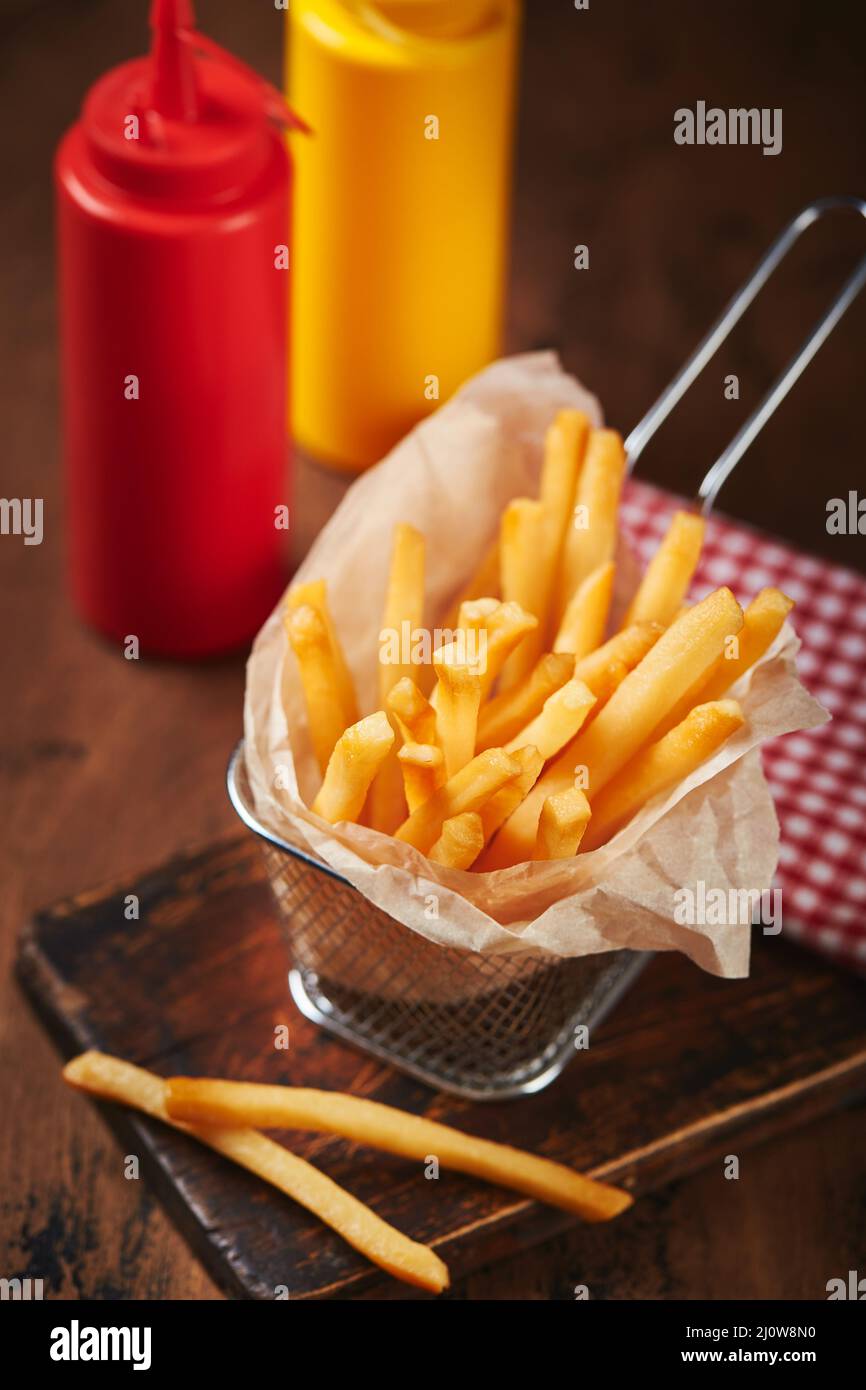 Frites dans un panier en maille de métal sur une planche de bois. Restauration rapide, cuisine américaine Banque D'Images