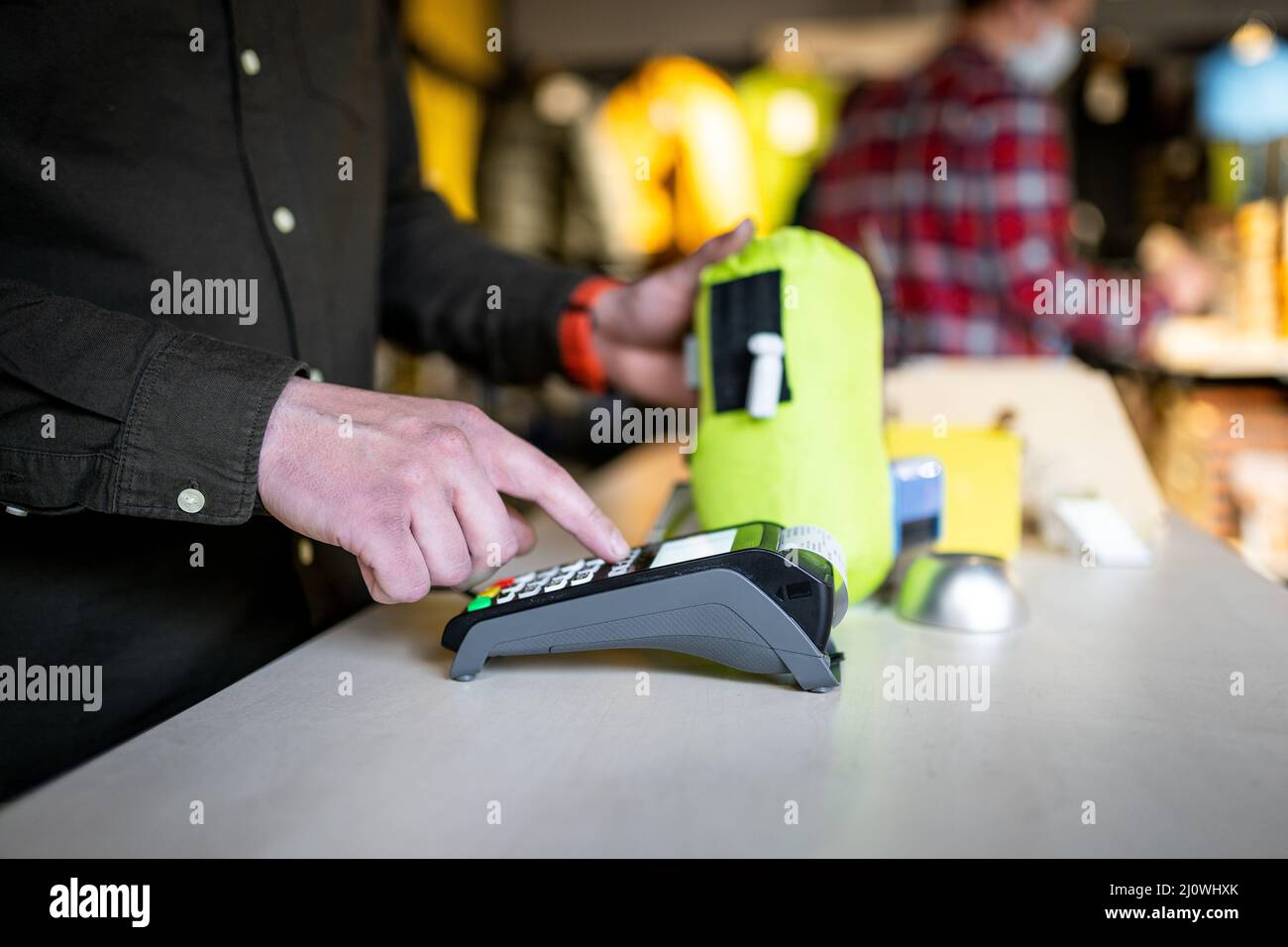 Gros plan des mains d'un vendeur caissière tenant le terminal du PDV et d'un reçu papier derrière le comptoir d'un magasin de sport. Env Banque D'Images