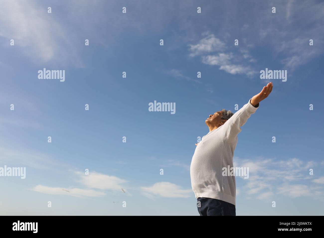 Vue à angle bas de l'homme biracial insouciant avec les bras s'étirent contre le ciel bleu le jour ensoleillé Banque D'Images