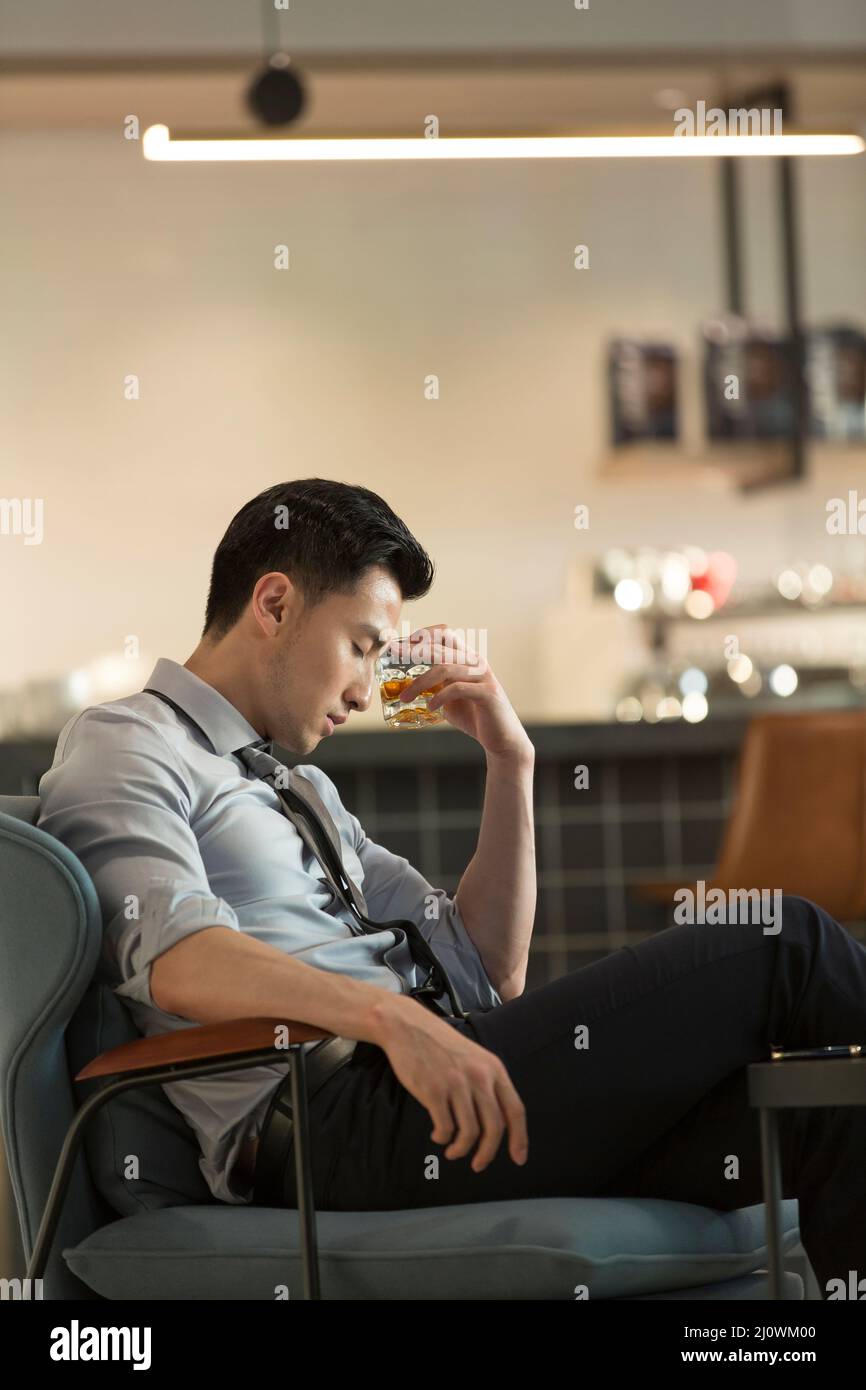 Un jeune homme d'affaires chinois fatigué boit de l'alcool et se détend au bar de l'hôtel Banque D'Images
