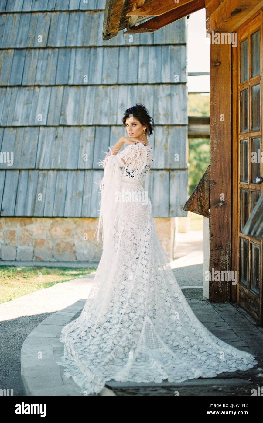 Mariée dans une longue robe blanche en osier se tient sur le seuil d'une maison en bois Banque D'Images