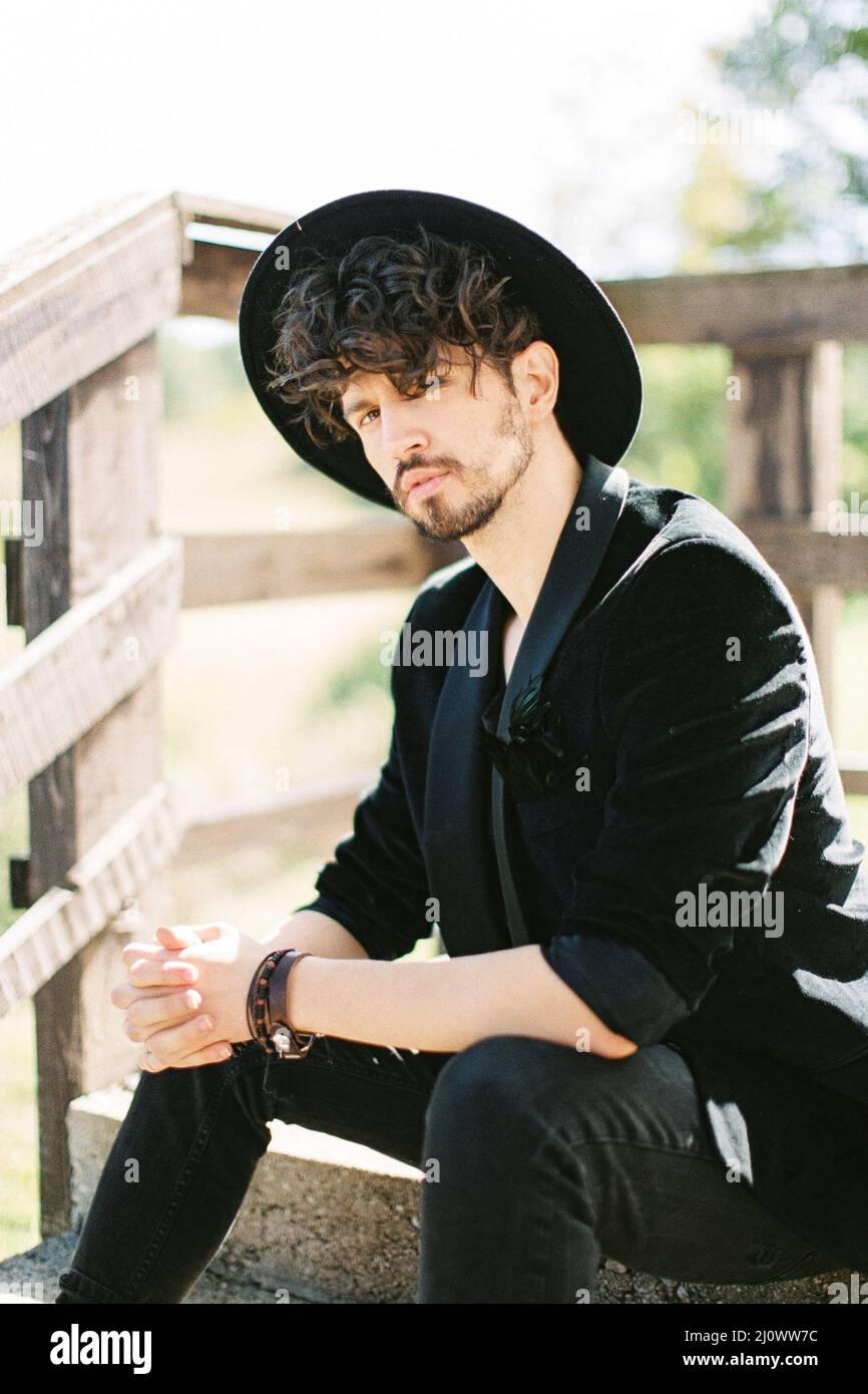 Homme dans un chapeau noir est assis sur les marches près de la main courante en bois Banque D'Images