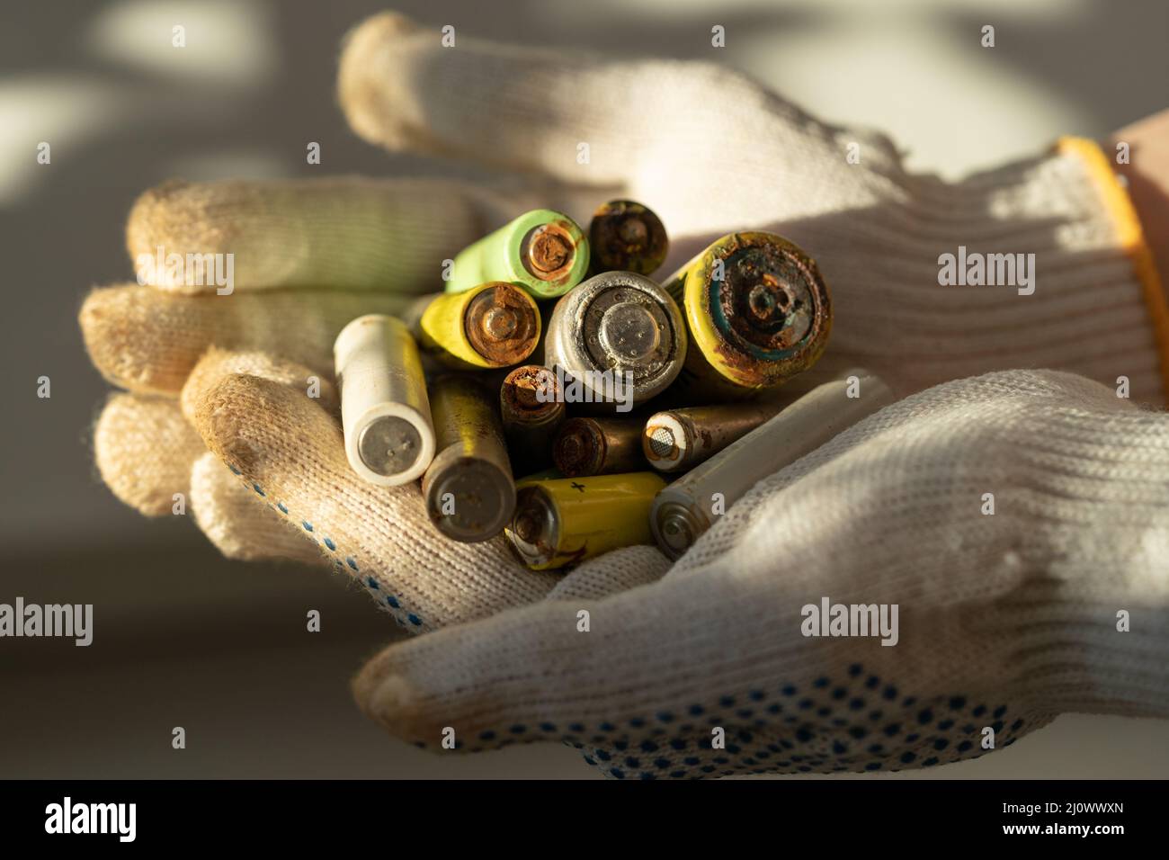 Gros plan des mains des femmes dans des gants de protection en coton tenant le tas de piles alcalines usagées Banque D'Images