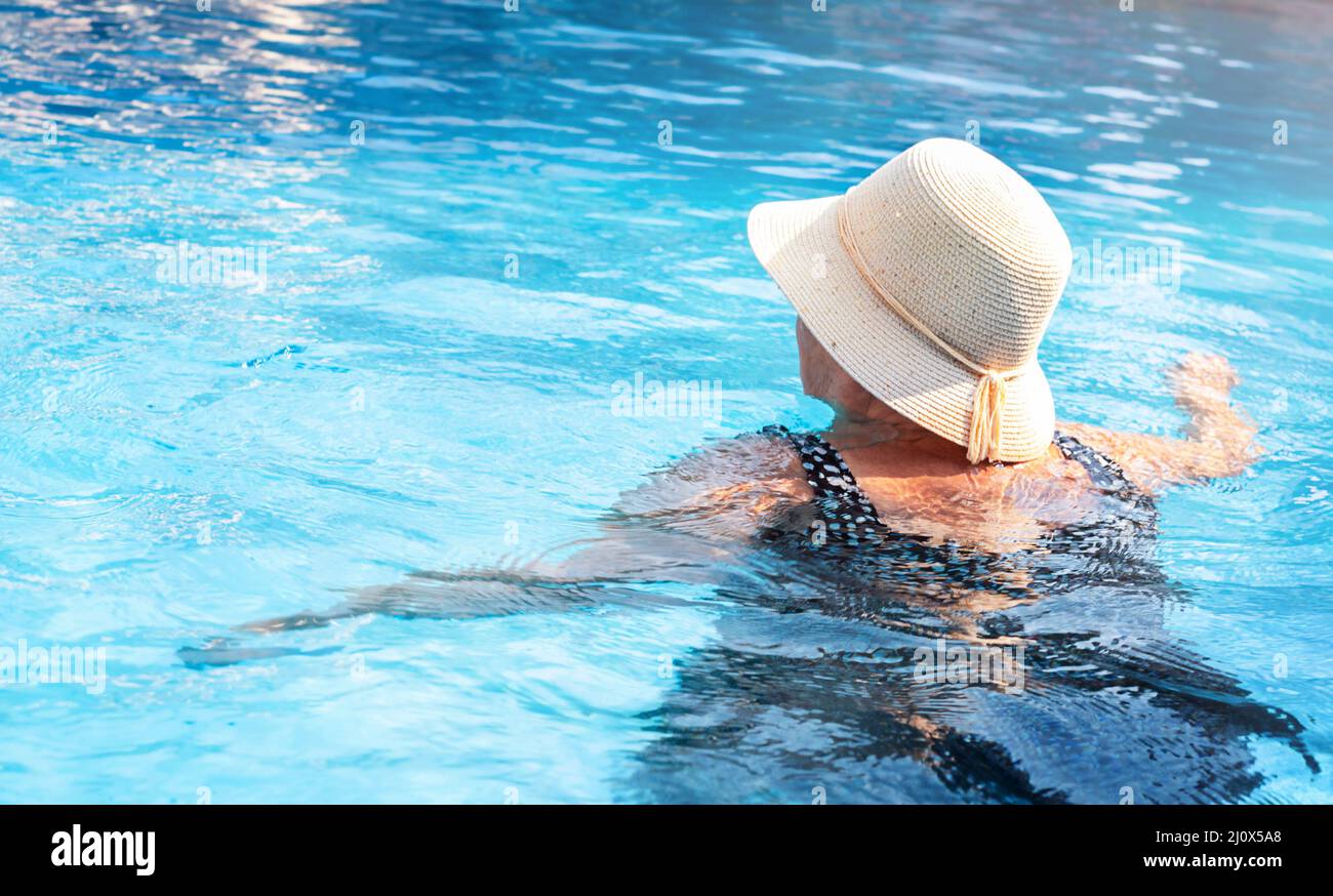 Femme active senior dans un chapeau nage dans la piscine en vacances Banque D'Images