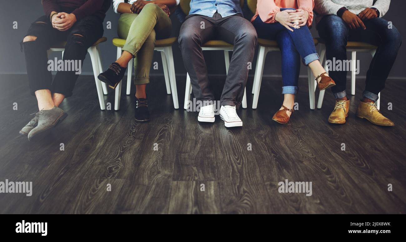 Les bonnes choses arrivent à ceux qui attendent. Petit studio photo d'un groupe de personnes attendant en ligne sur des chaises sur fond gris. Banque D'Images