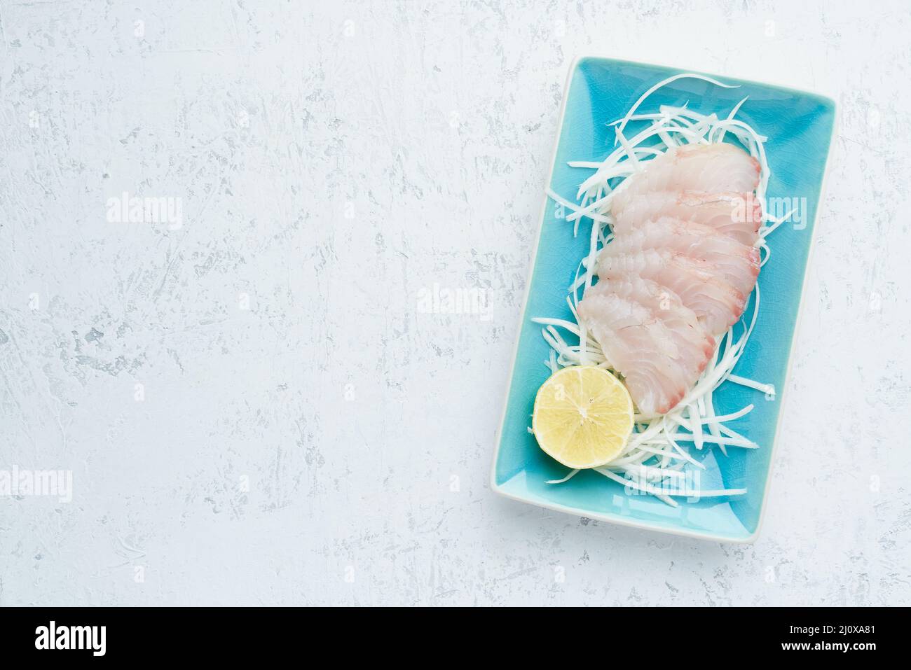 Sashimi à partir de tranches de filet de poisson blanc brut sur une plaque bleue sur fond blanc. Copier l'espace Banque D'Images