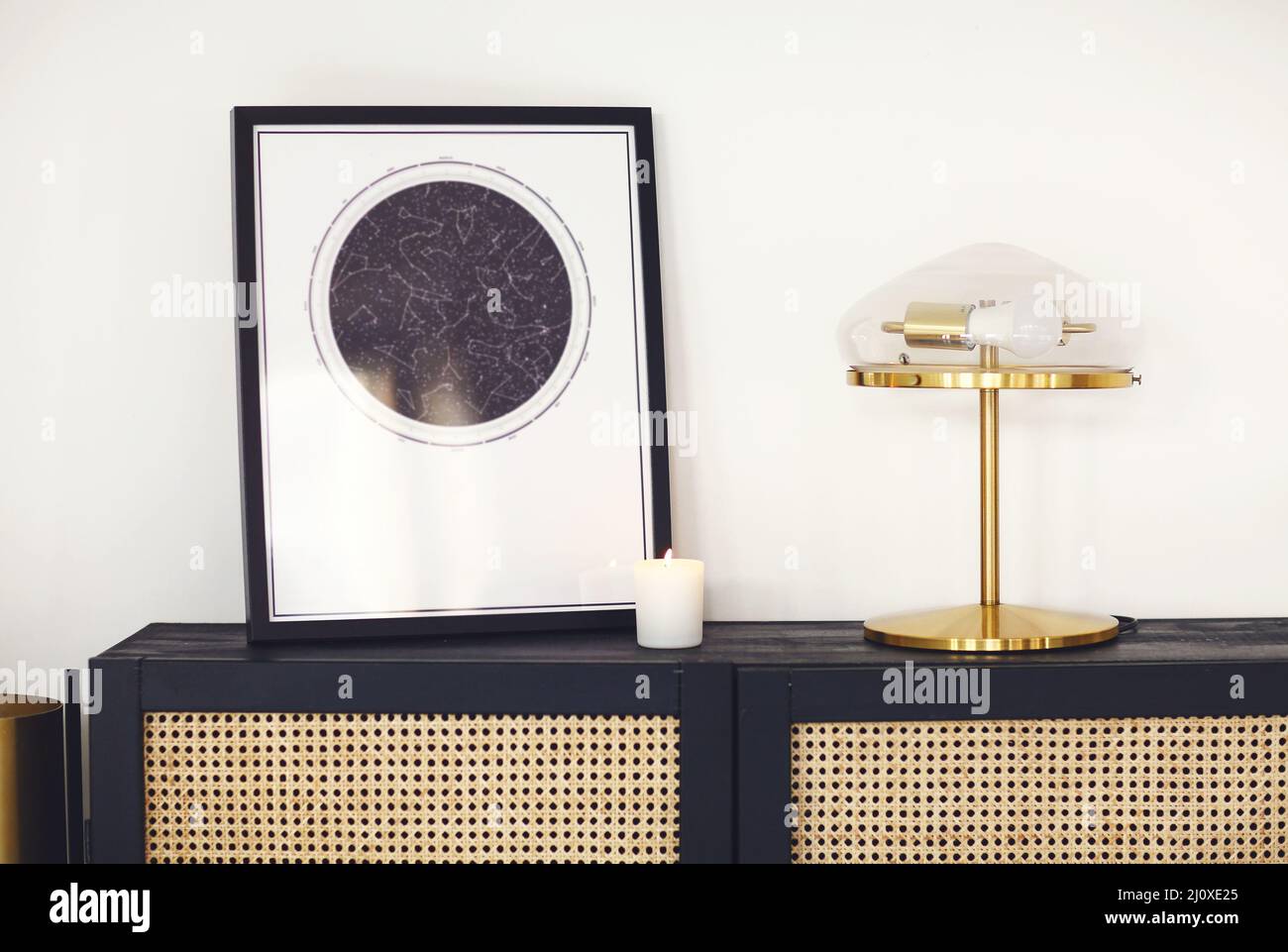 Commode en bois noir avec affiche carte encadrée d'étoiles, lampe et bougie dans un intérieur minimaliste Banque D'Images