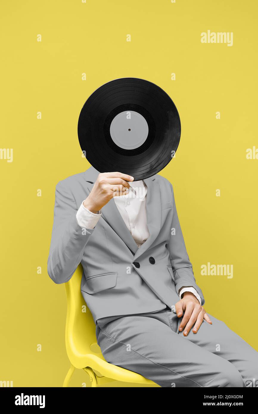 Homme couvrant son visage avec un disque en vinyle tout en portant des vêtements gris ultimes. Photo de haute qualité Banque D'Images