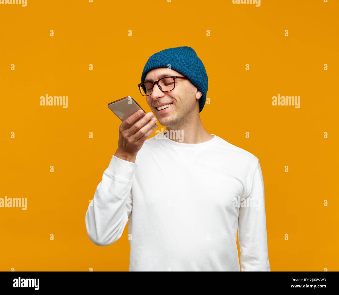 Portrait d'un jeune homme positif enregistrant un message audio, parlant au microphone du téléphone portable Banque D'Images