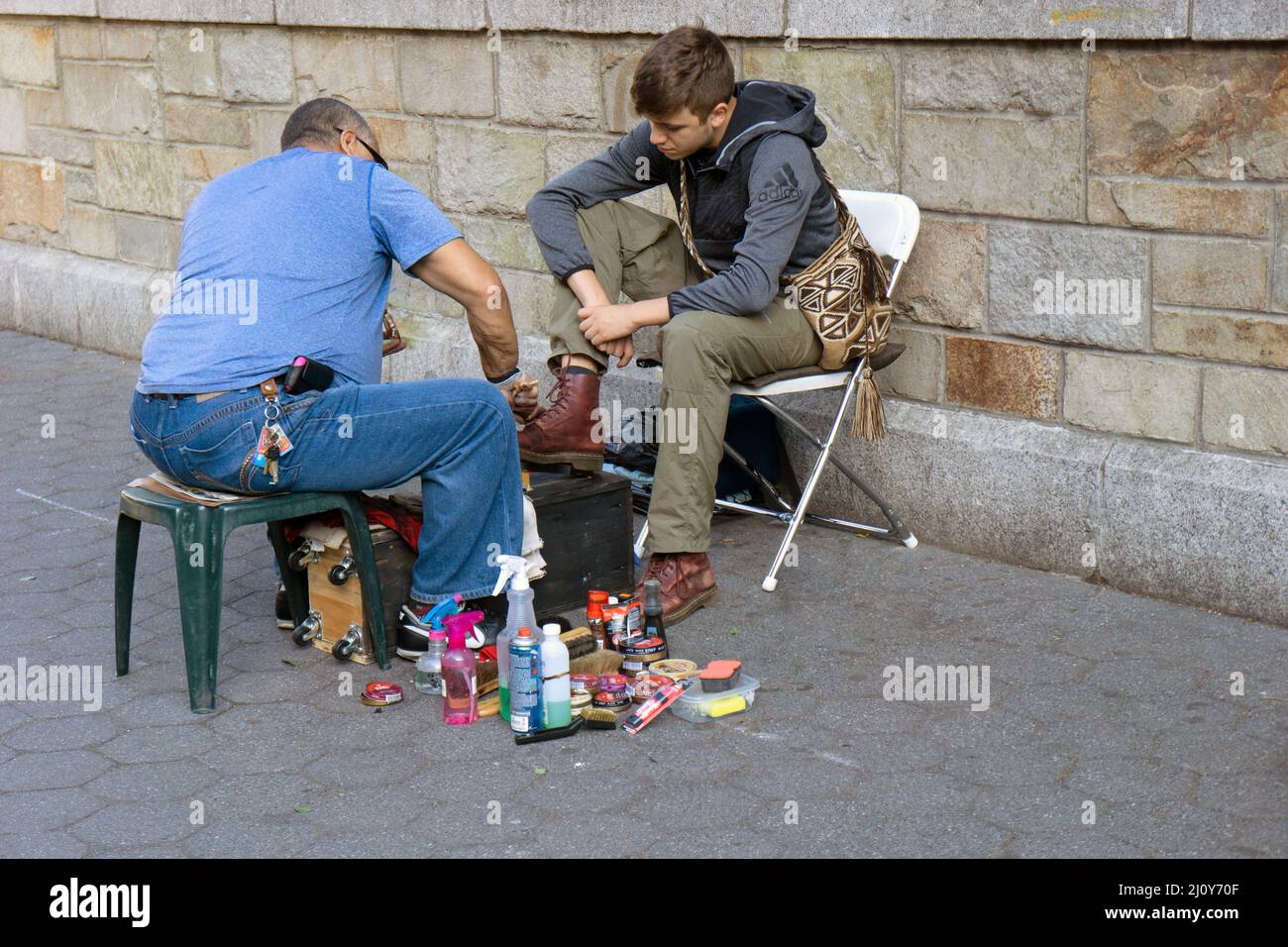 Un briller shone d'âge moyen a poli les bottes Doc Marten d'un jeune homme à Union Square Park à Manhattan, New York. Banque D'Images