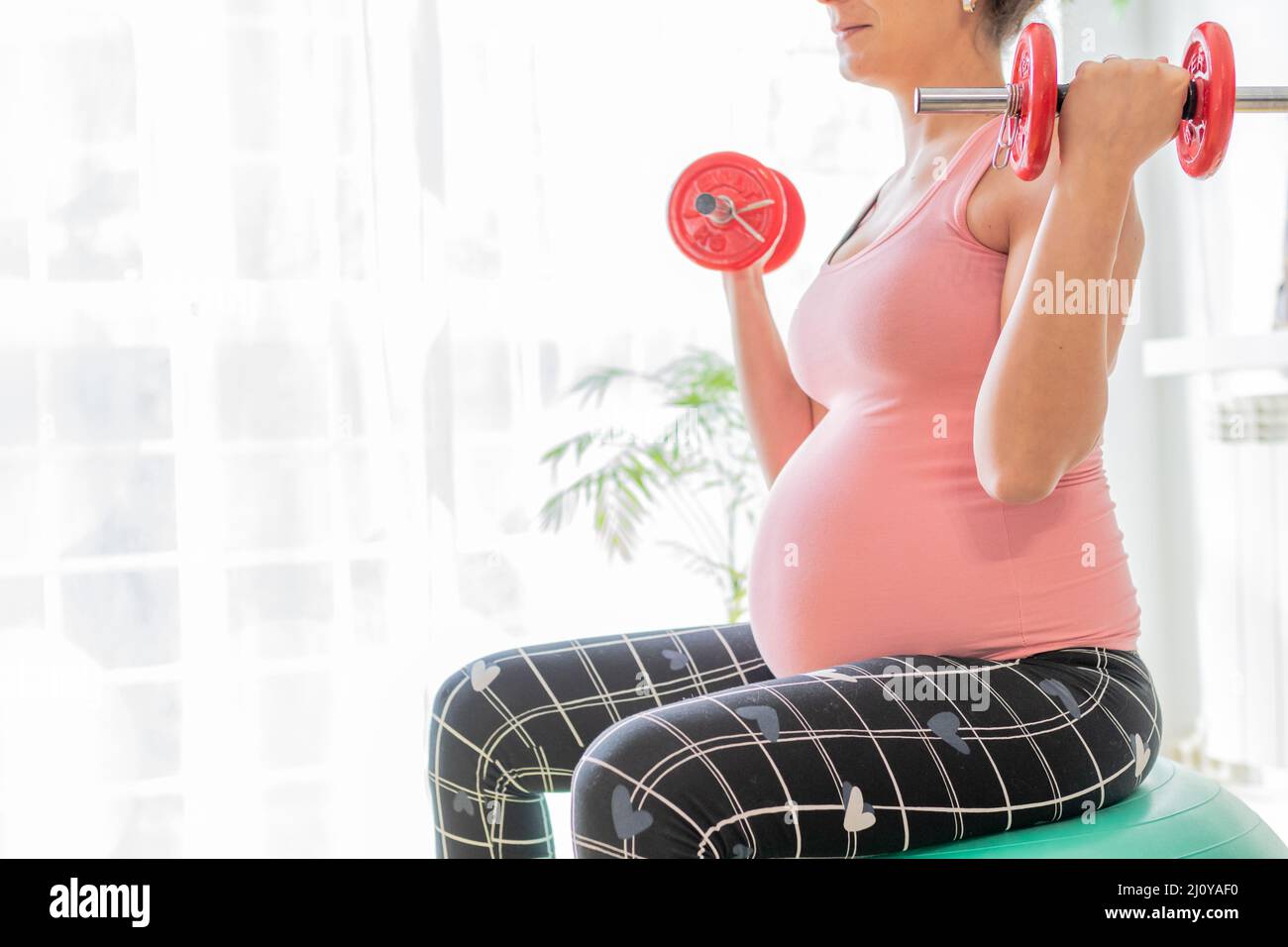 jeune femme enceinte levant des haltères assis sur une balle de fitness. soins de santé et de corps et exercices pendant la grossesse Banque D'Images
