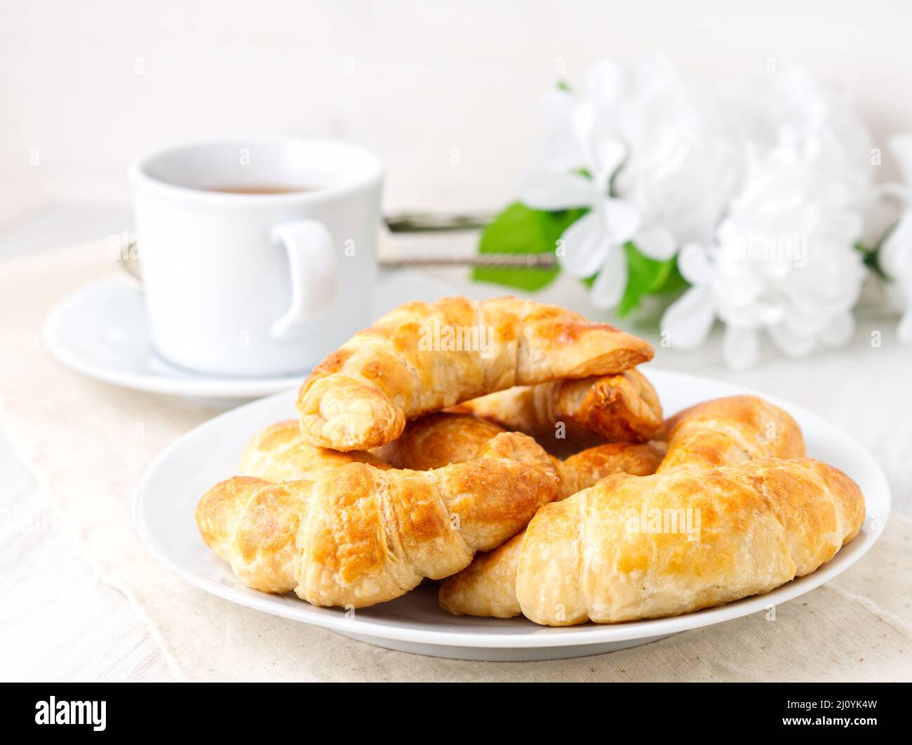 Tasse de thé, fleurs et pâte feuilletée fraîche sur une table blanche. Délicieux croissants, vue latérale Banque D'Images