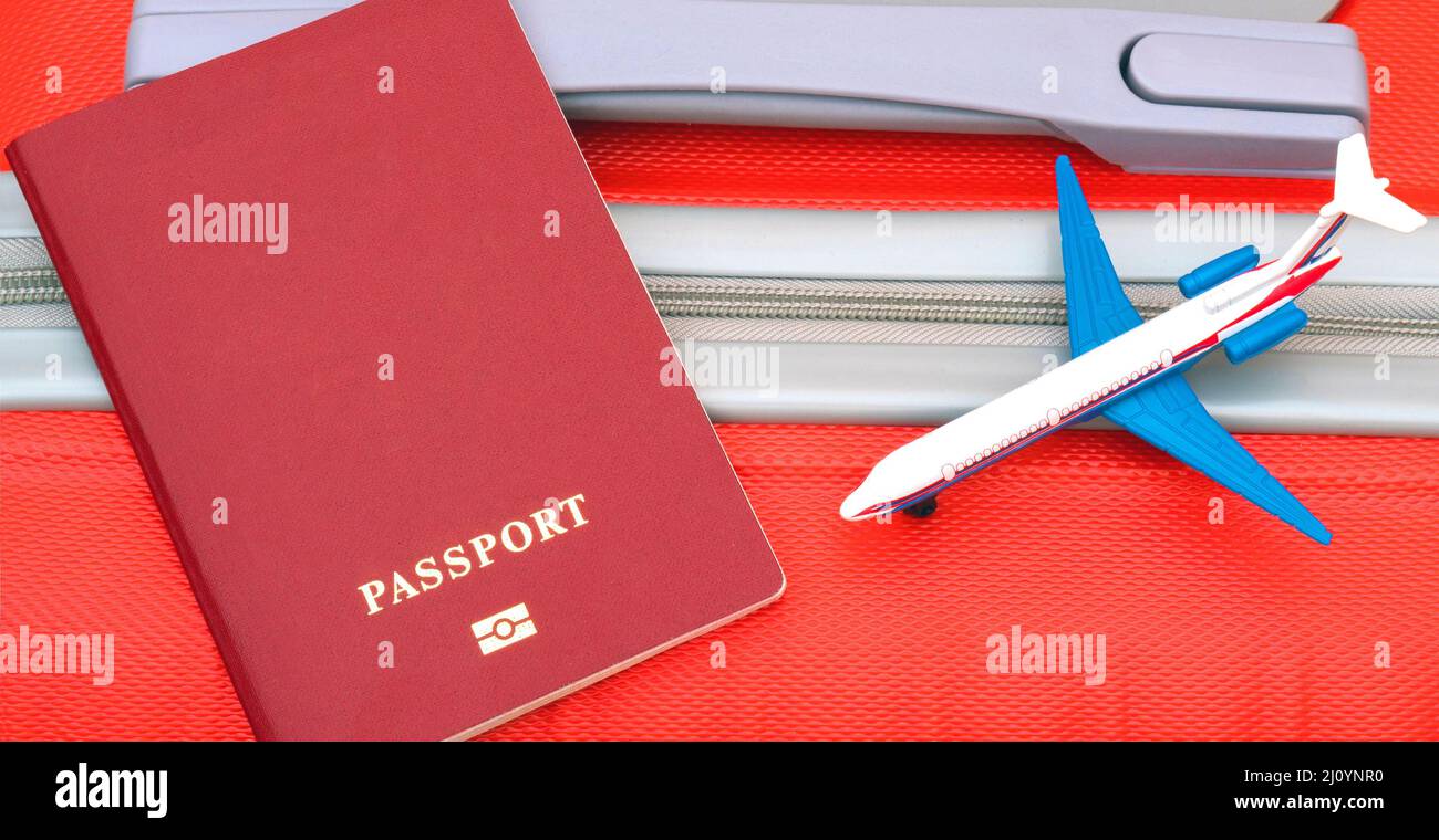 Un passeport rouge et un modèle d'avion se trouvent sur une valise rouge. Voyager dans le monde en avion. Banque D'Images