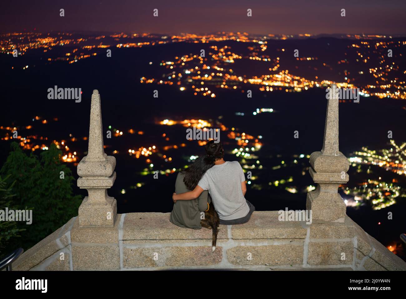 Couple s'embrassant avec un chien sur un point de vue en pierre antique regardant les lumières de la ville de nuit Banque D'Images