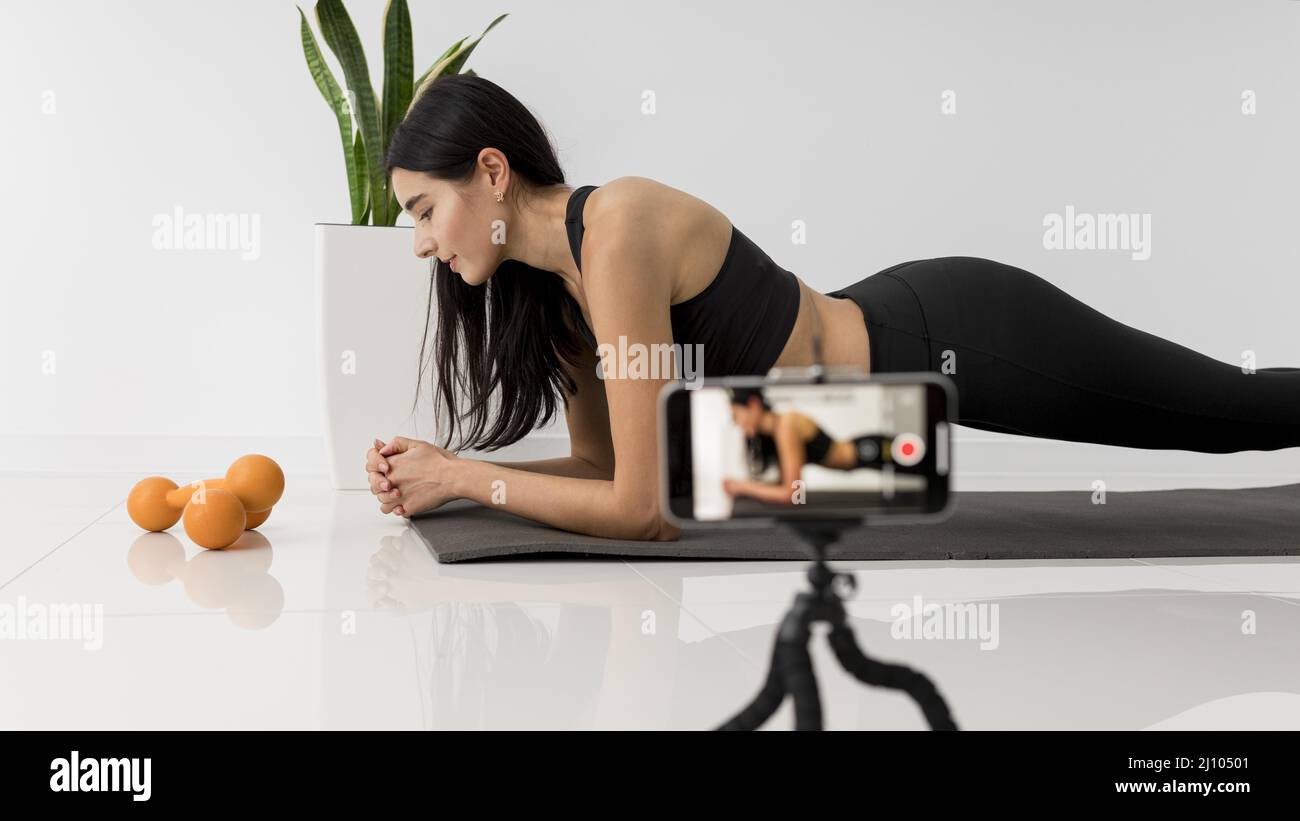 Une femme influenceur se vjournalisation à domicile lors de ses exercices avec son smartphone Banque D'Images