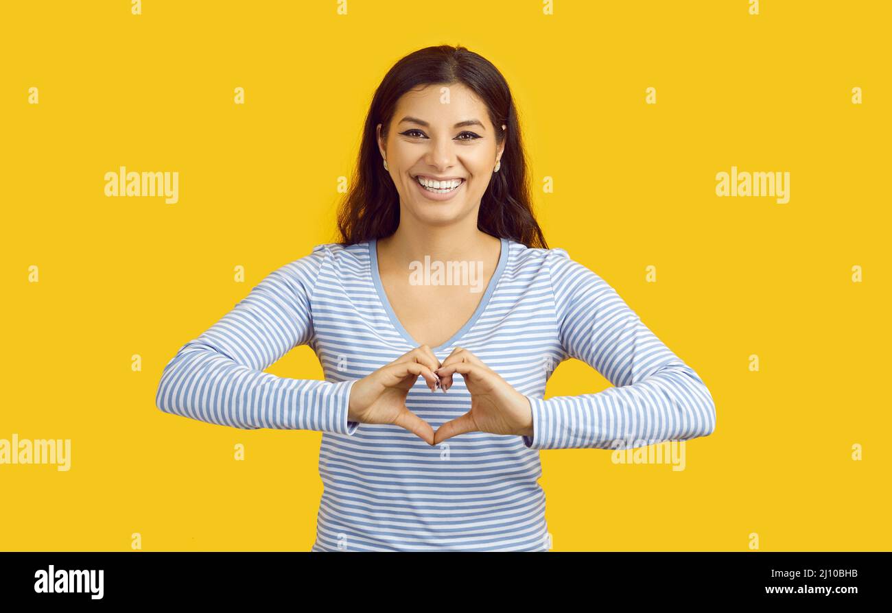 Joyeuse jeune femme drôle montrant le geste d'amour isolé sur fond jaune vif. Banque D'Images