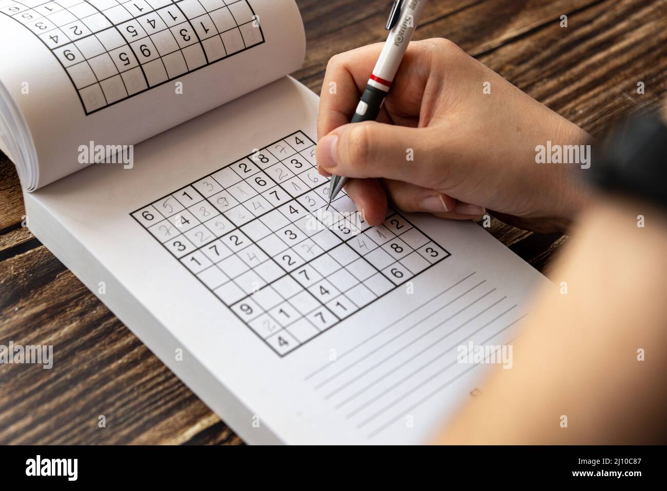 Personne résolvant un puzzle de sudoku sur une table en bois Banque D'Images