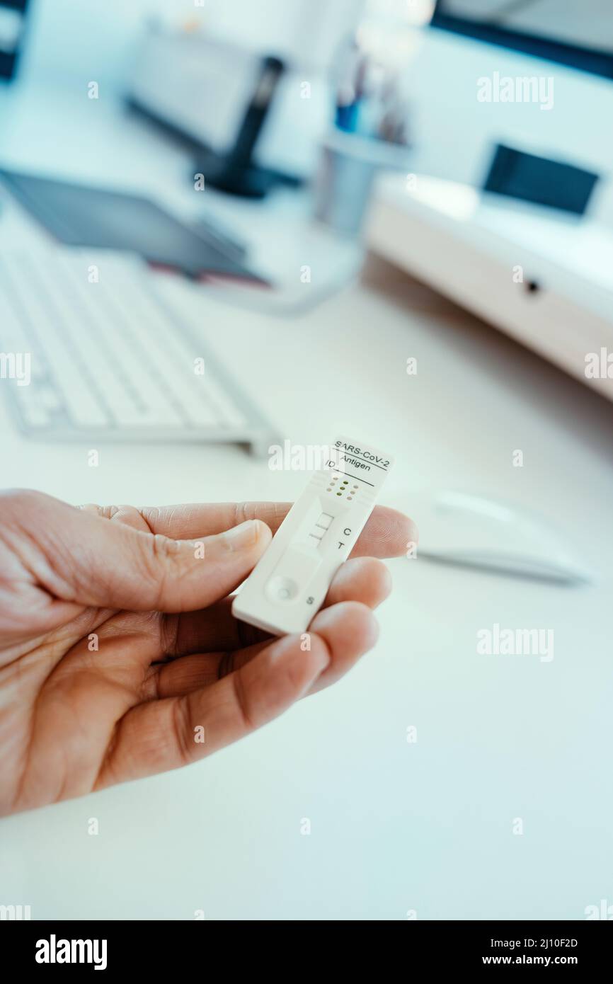 gros plan d'un homme au bureau avec un dispositif de test diagnostique d'antigène covid-19 avec un résultat positif dans la main Banque D'Images