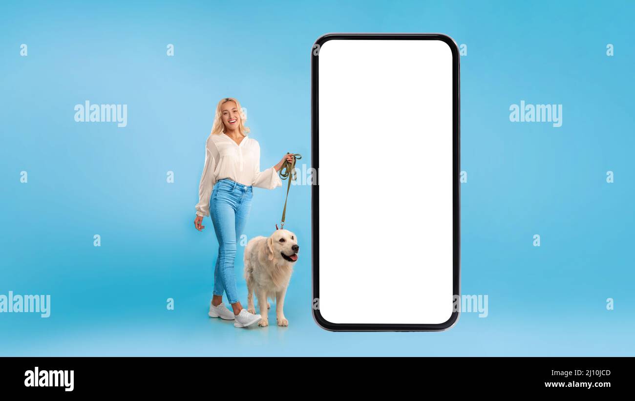 Jeune femme marchant son chien près d'un grand smartphone Banque D'Images