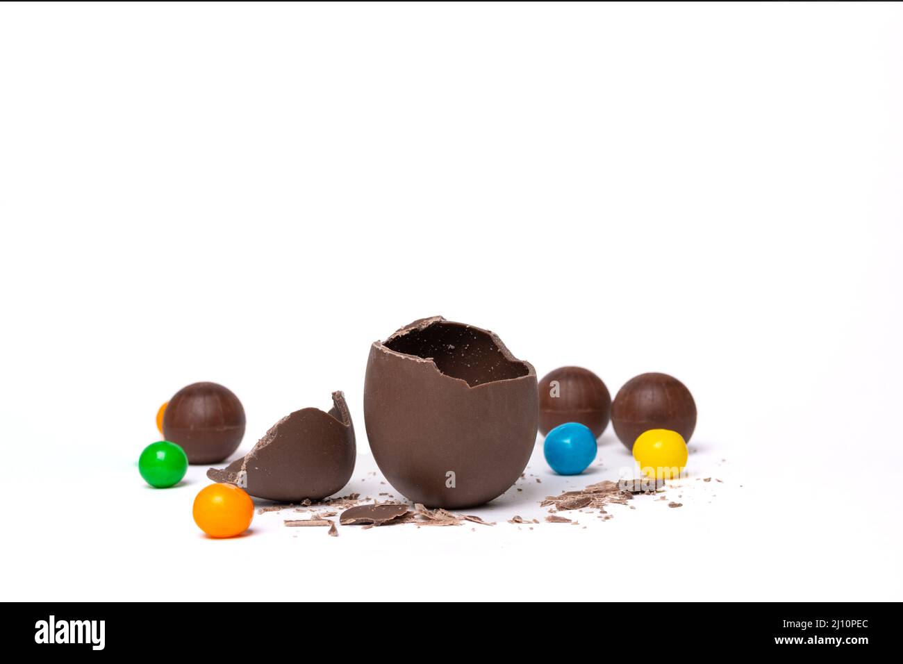 Œuf de pâques vide au chocolat craqué et bonbons ronds au chocolat colorés sur fond blanc, espace de copie. Chocolat pour les enfants. Concept de Pâques. Banque D'Images