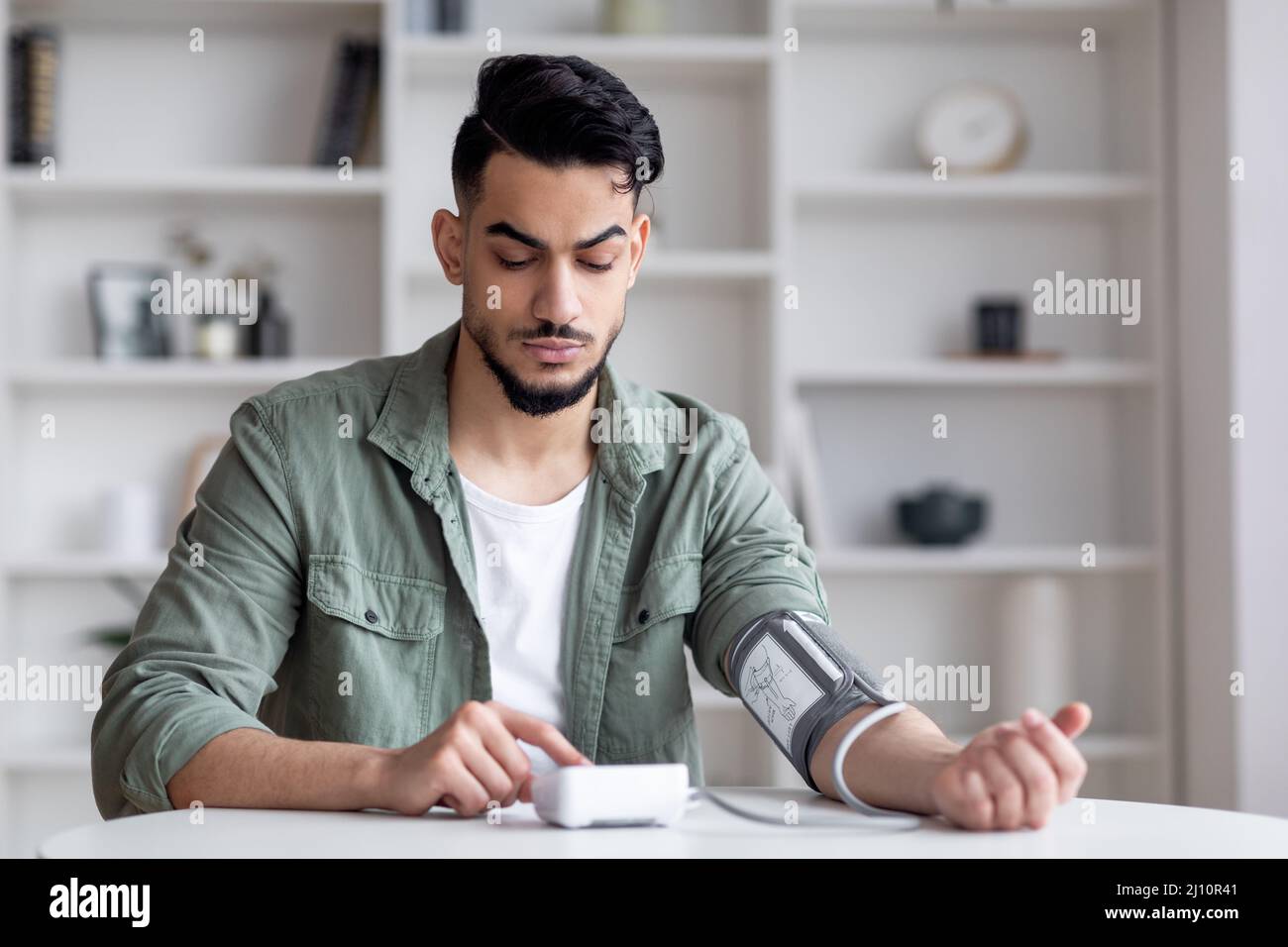 Jeune homme arabe contrôle de la pression artérielle avec le tonomètre moderne à la maison Banque D'Images