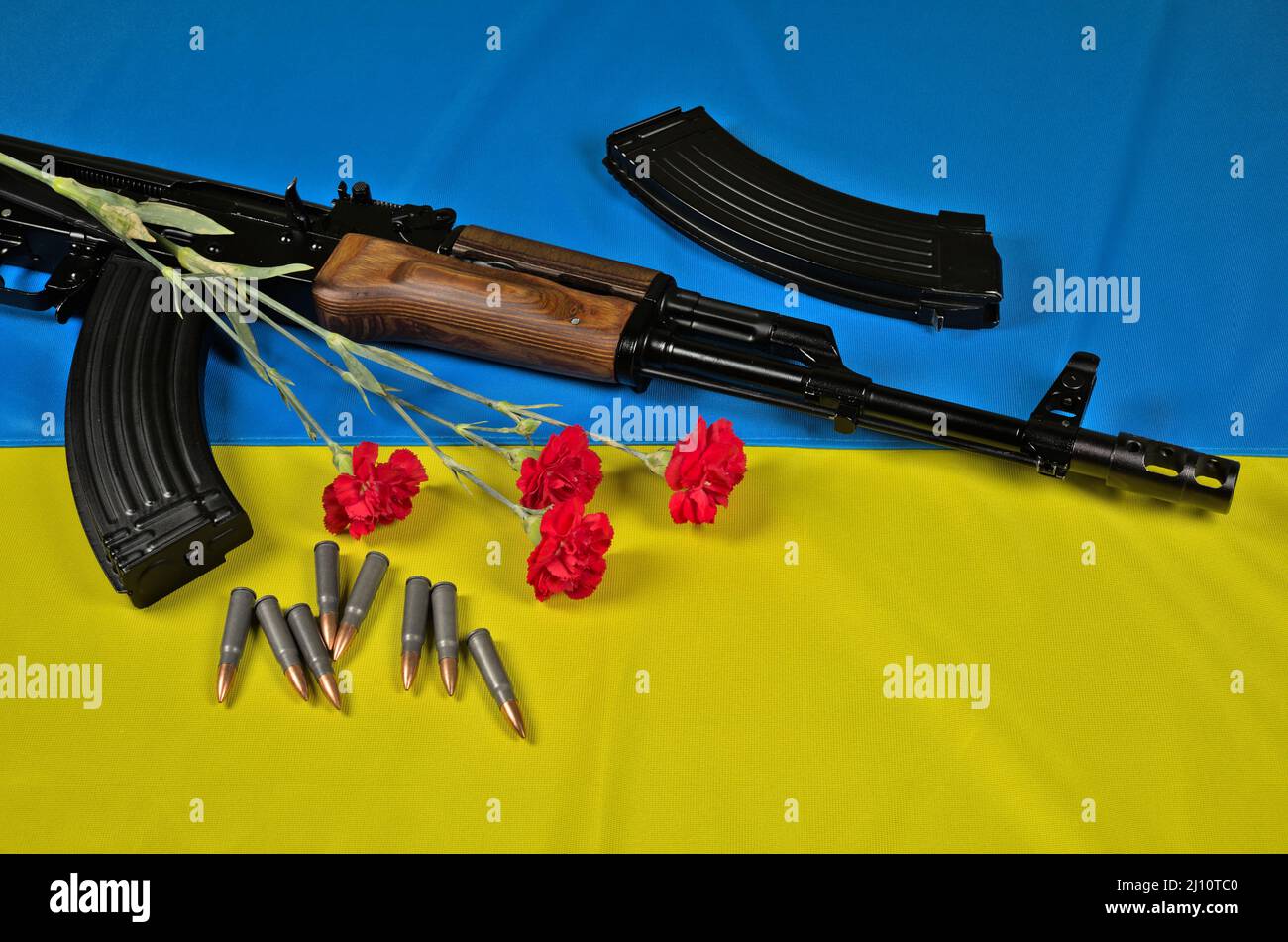 AK-47 fusil, magazines, munitions et fleur rouge de la carnation sur un drapeau ukrainien bleu-jaune Banque D'Images