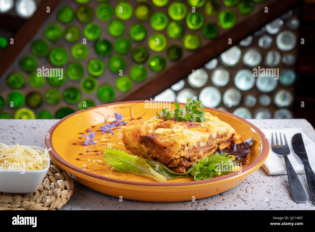 lasagnes sur une assiette orange accompagnées de feuilles de laitue, de cresson et de fleurs violettes. Banque D'Images