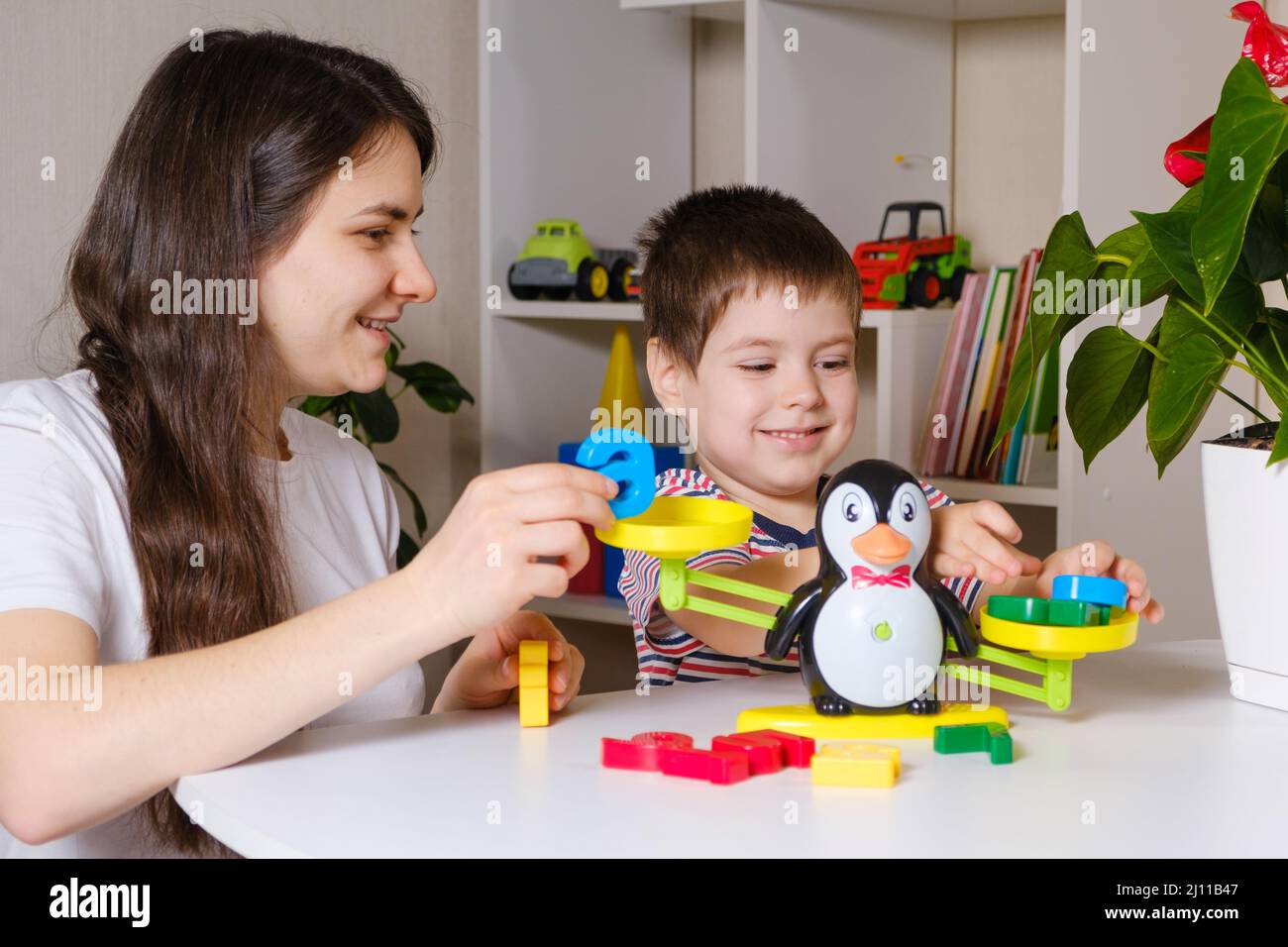 Maman et fils jouent avec des nombres, pèsent un pingouin sur une balance de jouet. Banque D'Images