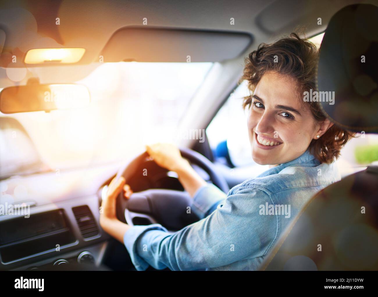 Vous êtes maintenant sur le siège du conducteur. Portrait d'une jeune femme heureuse conduisant une voiture. Banque D'Images