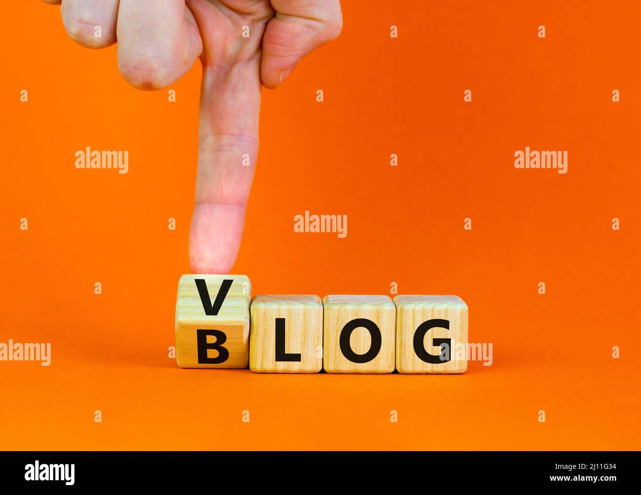 Blog ou symbole Vlog. Homme d'affaires tourne des cubes en bois et change le mot Blog à Vlog. Belle table orange fond orange. Business et informat Banque D'Images