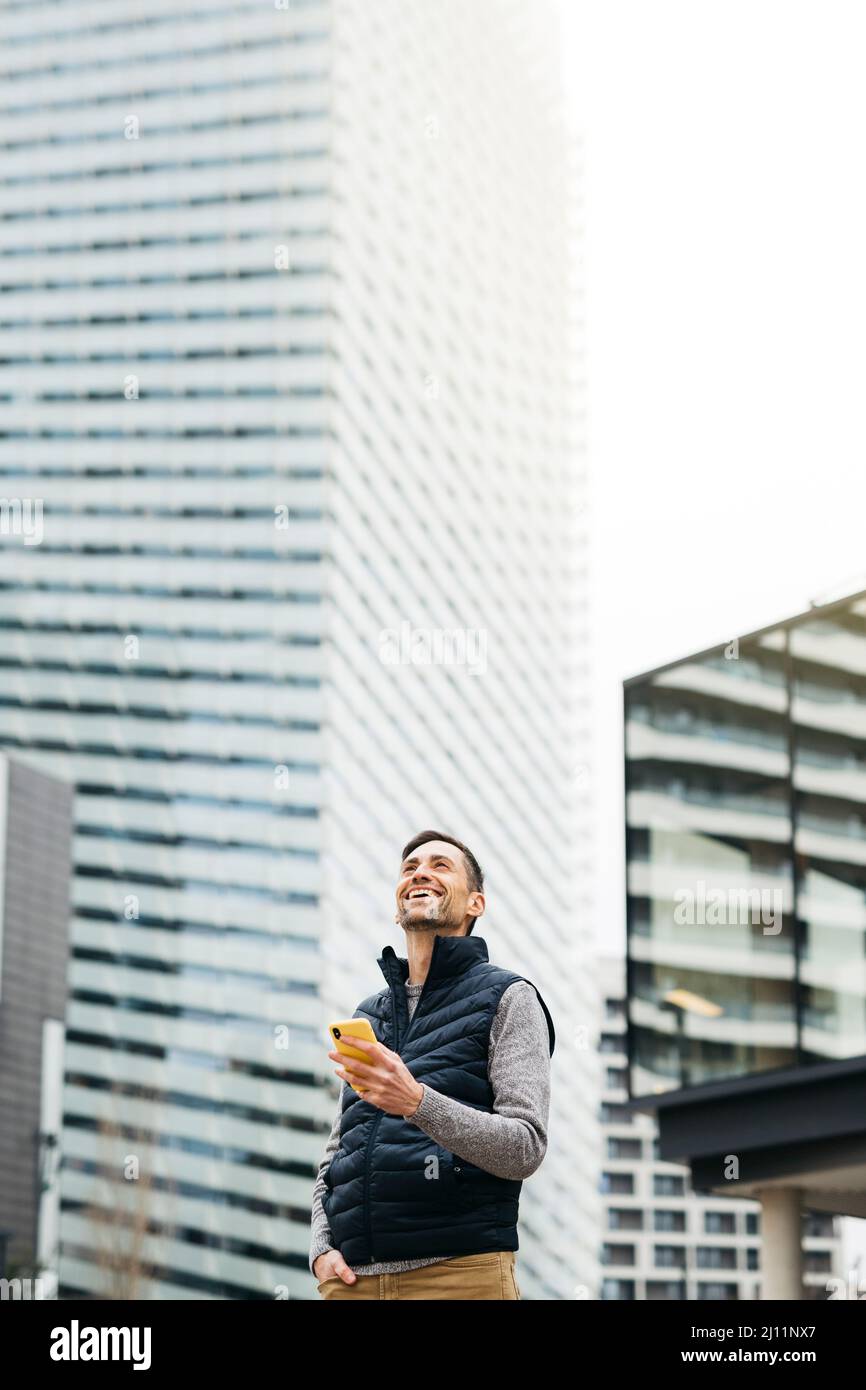 Indépendant homme dans des vêtements décontractés, utilisant un smartphone, bâtiment moderne sur fond. Travailler à distance en milieu urbain Banque D'Images