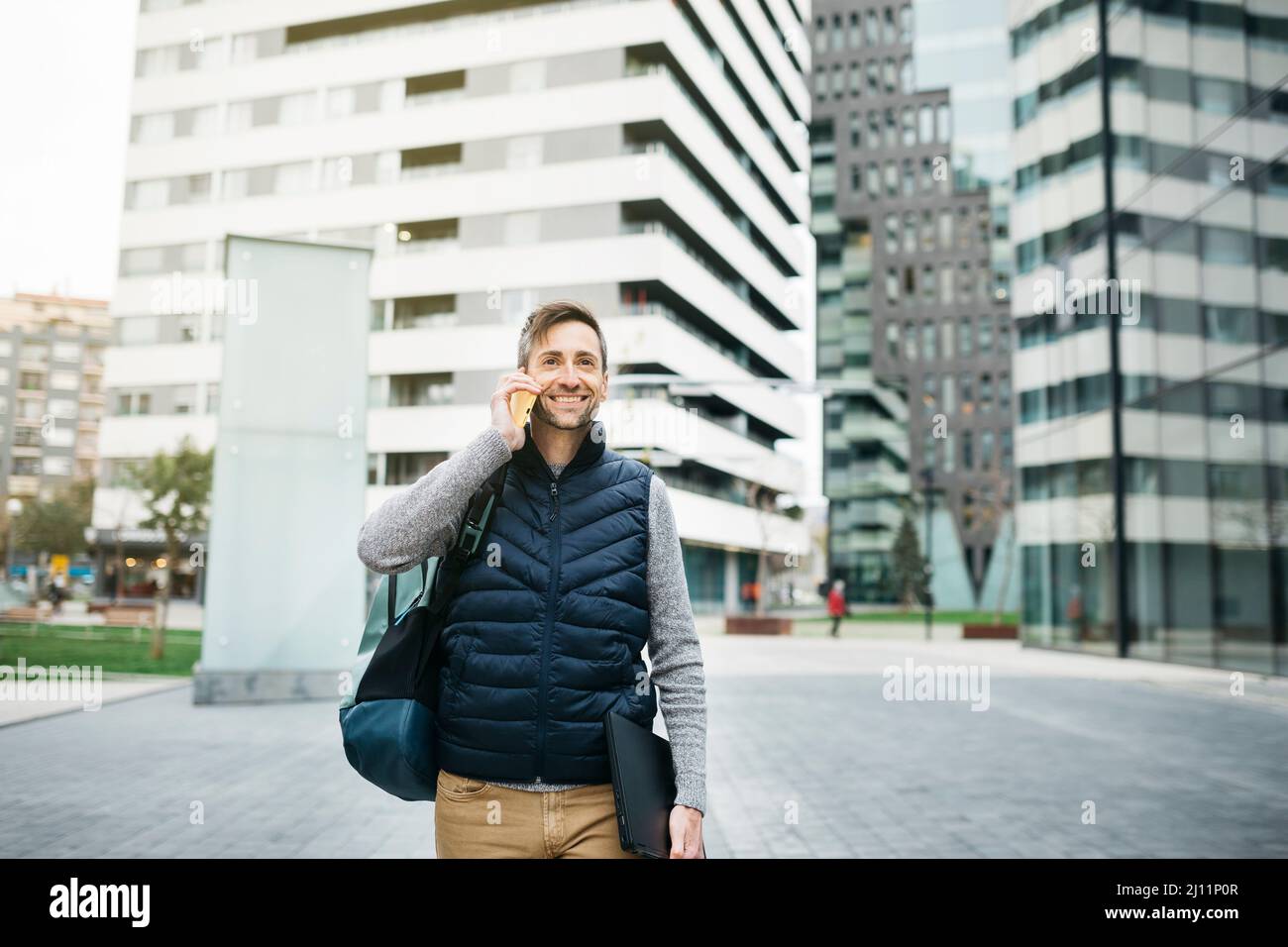 Indépendant homme dans des vêtements décontractés, utilisant un smartphone, bâtiment moderne sur fond. Travailler à distance en milieu urbain Banque D'Images