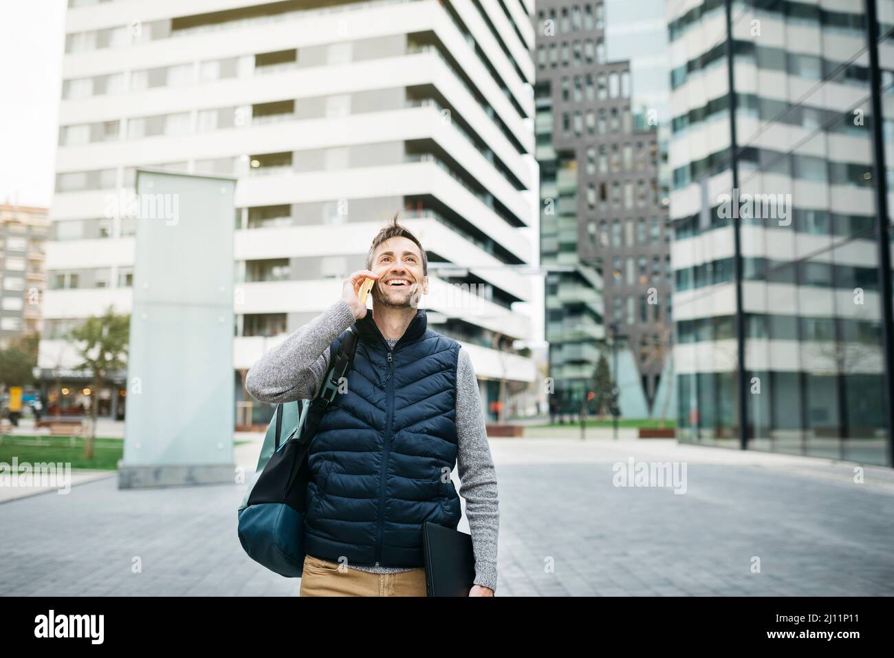 Indépendant homme dans des vêtements décontractés, utilisant un smartphone, bâtiment moderne sur fond. Travailler à distance en milieu urbain Banque D'Images