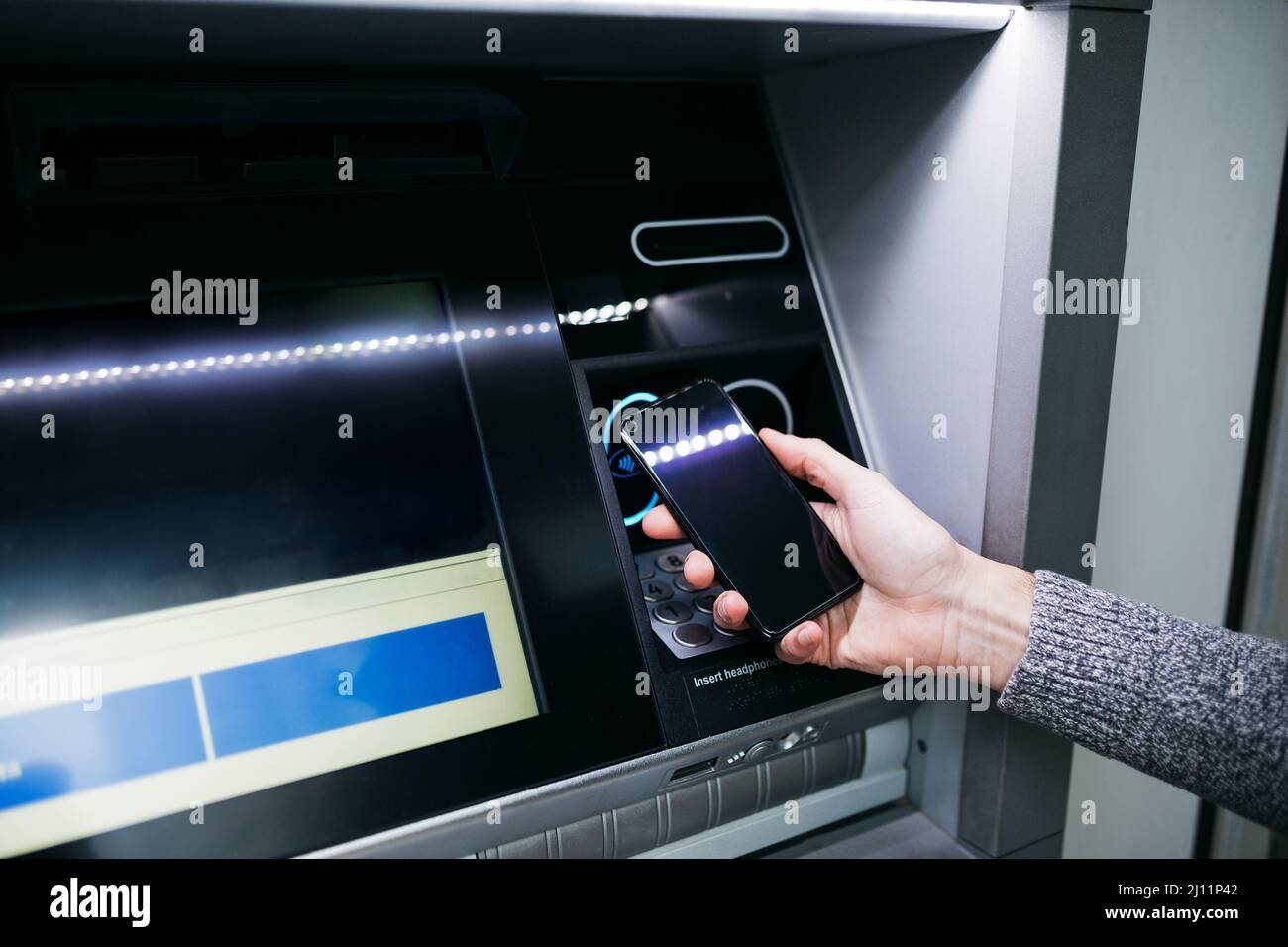 Main de l'homme avec un smartphone utilisant un distributeur automatique de rue pour retirer de l'argent Banque D'Images