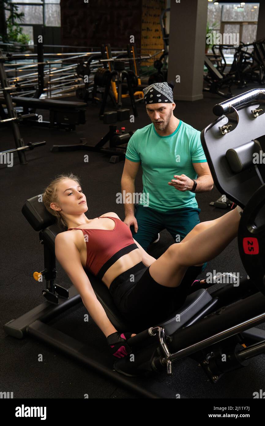 L'entraînement dirigé par un instructeur aide un beau client à effectuer des exercices dans un club de remise en forme, le concept de jouer du sport avec un loisir professionnel de gym Banque D'Images