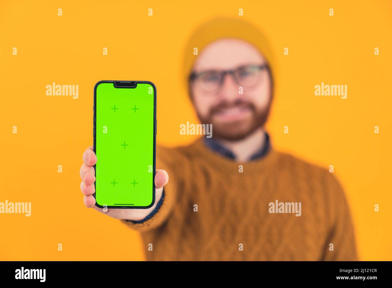 Jeune souriant caucasien barbu homme montrant l'affichage vertical de son téléphone à la caméra sélective se concentre sur le téléphone décontracté vêtements orange arrière-plan isolé studio tourné . Photo de haute qualité Banque D'Images